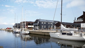 A marina with several sailboats docked, a modern building with a sloped roof, and a person cycling on the dock. - 8 Person Holiday Home on a Holiday Park in Bogense (Bogense)