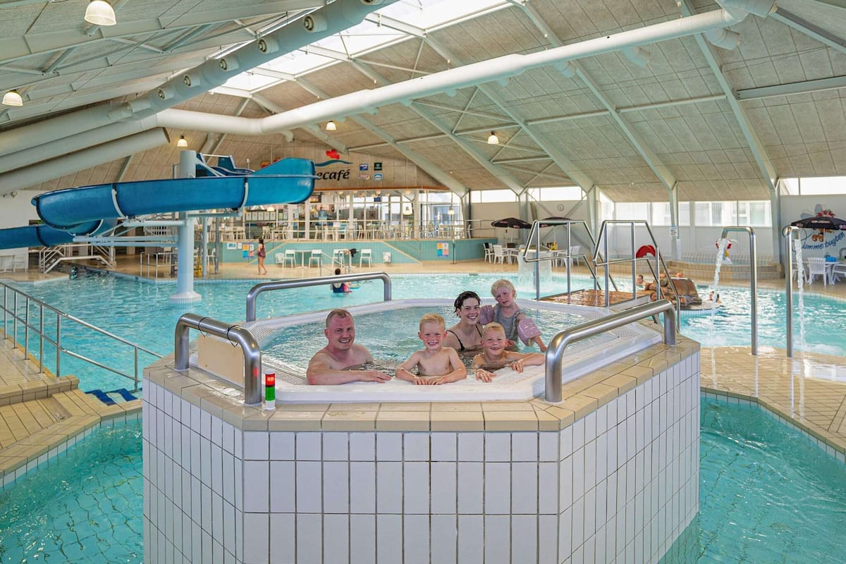 Une piscine intérieure avec un espace jacuzzi, des chaises longues et un café en arrière-plan.
