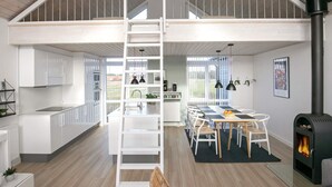 Een moderne loft-achtige woonruimte met een centrale trap, open keuken, eethoek en een houtkachel.