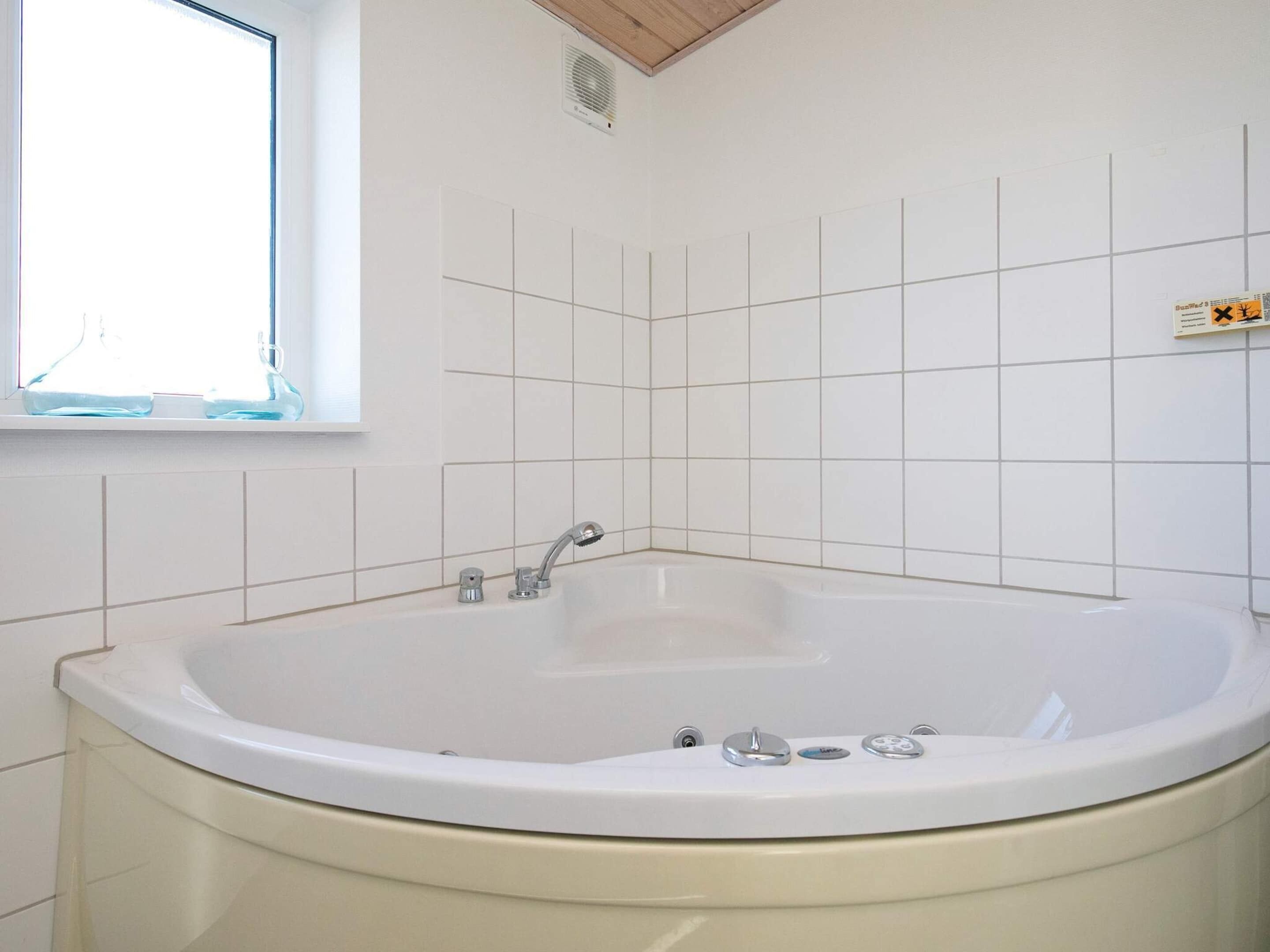 A bathroom with a freestanding bathtub, a window, and white tiled walls.