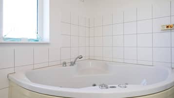 A bathroom with a freestanding bathtub, a window, and white tiled walls.