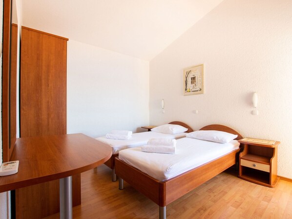 A hotel room with two wooden beds, a wooden desk, and a small bedside table.