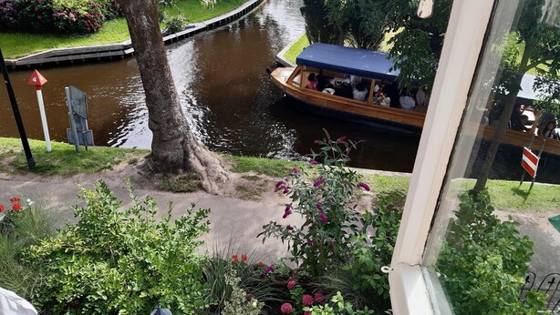 A canal with a boat carrying passengers, surrounded by lush greenery and a building in the background. - Lodge in Giethoorn With Breakfast (Giethoorn)