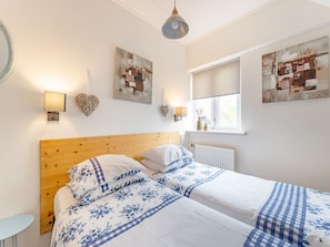 Ein Schlafzimmer mit einem Holzkopfteil, zwei Betten mit floralem Bettbezug, Wandleuchten und Kunstwerken.