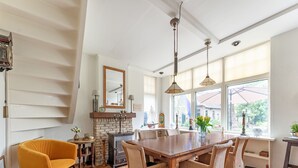 A dining area with a wooden table and wicker chairs, a fireplace, and large windows with an umbrella. - Lodge in Giethoorn With Breakfast (Giethoorn)