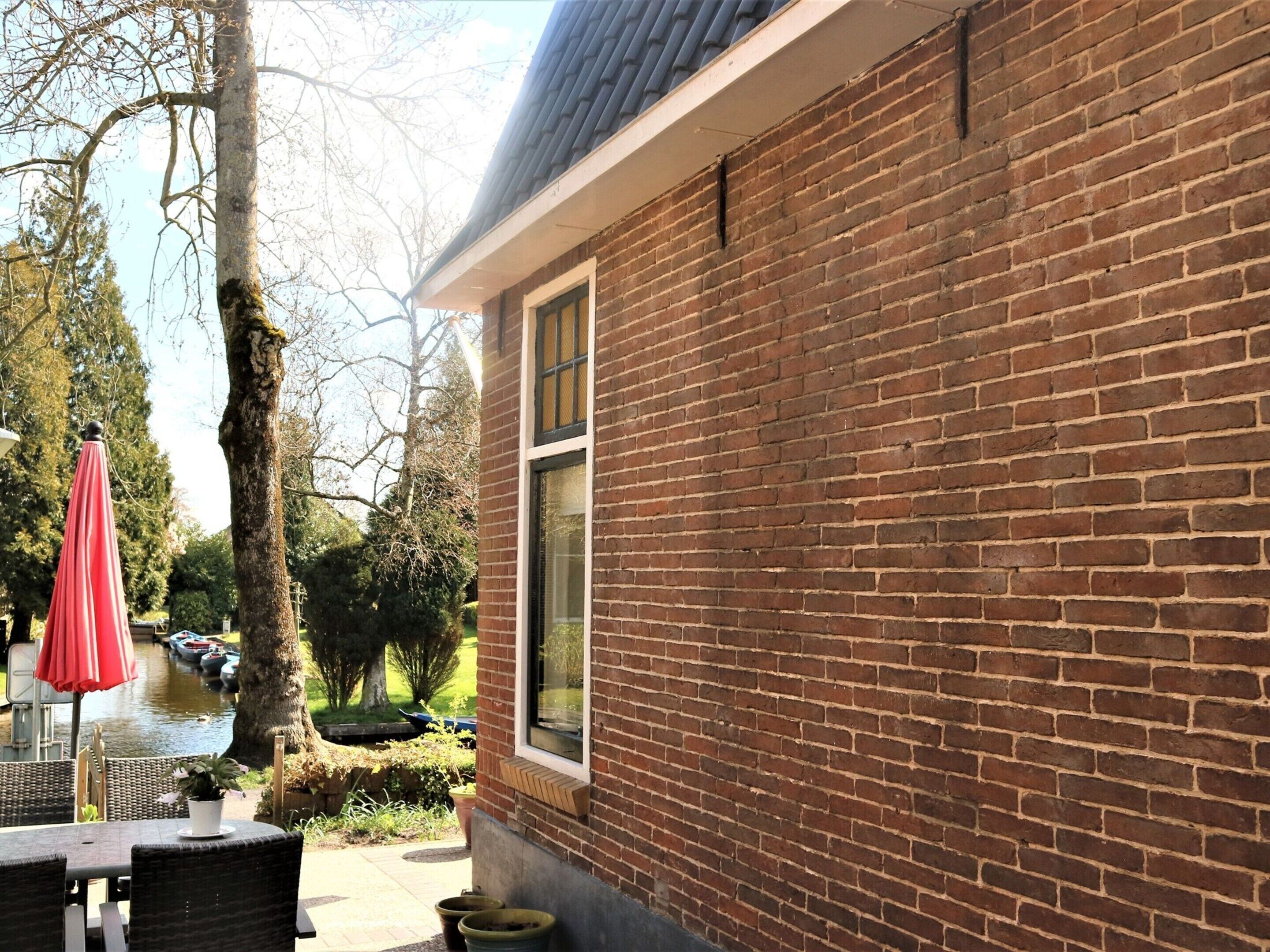 Ein Backsteinhaus mit einem Fenster, einer Terrasse mit Korbmöbeln und einem roten Sonnenschirm.