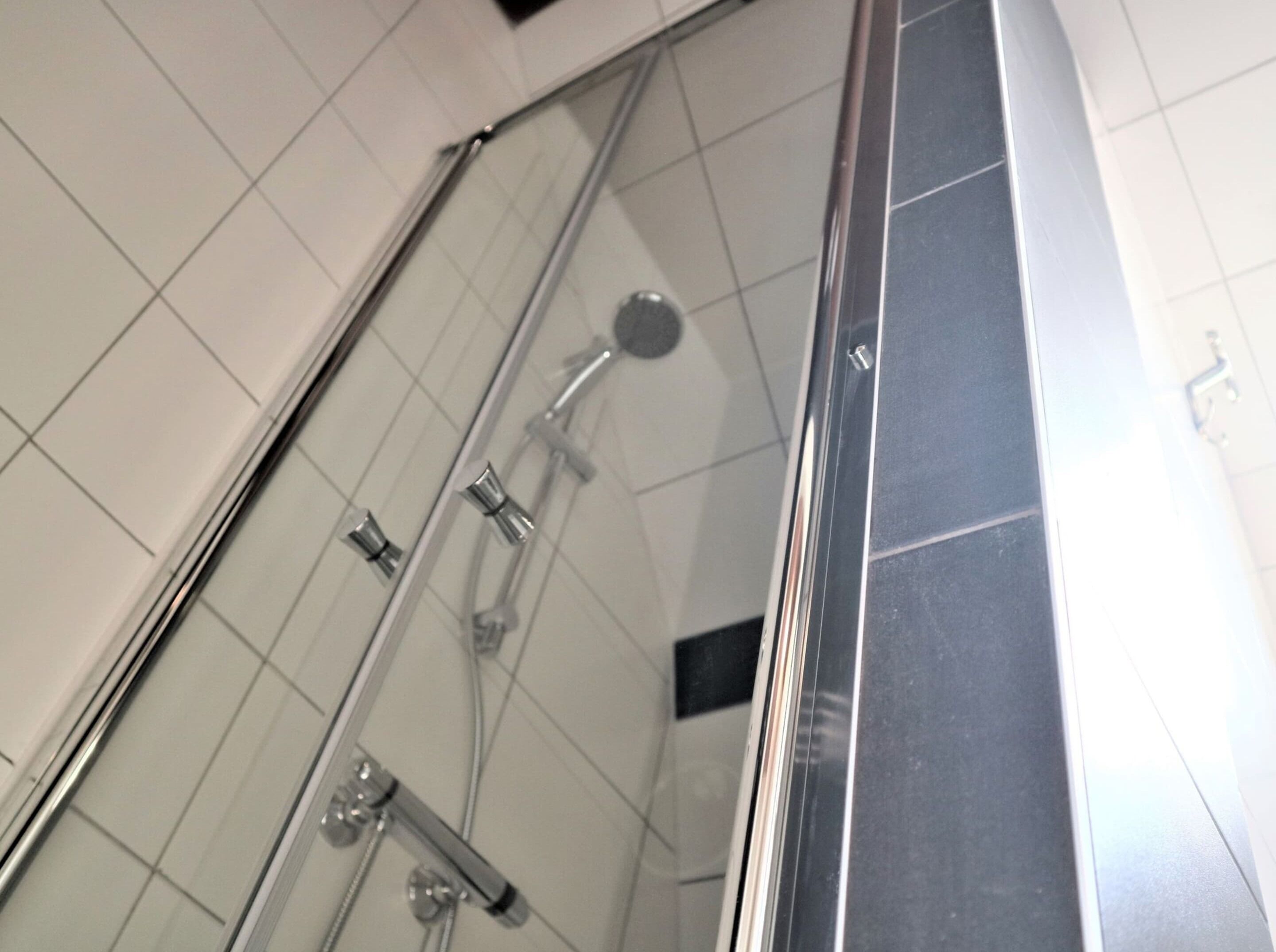 A shower with a glass door, chrome fixtures, and tiled walls.
