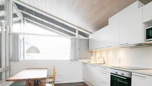 A modern kitchen with white cabinetry, a brick-patterned floor, and a dining area with a table and chairs. - 6 Person Holiday Home on a Holiday Park in Hanstholm (Hanstholm)