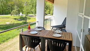 Una terraza de madera con una mesa preparada para dos, con vistas a una zona ajardinada con árboles.
