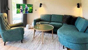 Una sala de estar moderna con un sofá verde, un sillón verde, una mesa de centro redonda y un televisor de pantalla plana montado en la pared.