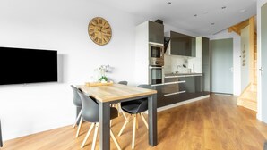 A modern kitchen with built-in appliances, a dining area with a wooden table and chairs, and a wall-mounted clock. - Attractive Holiday Home in Gorp and Roovert Estate (Goirle)