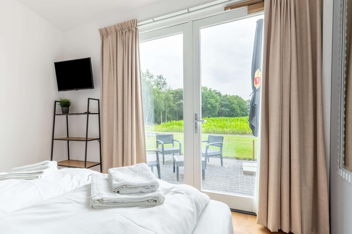 Ett hotellrum med en säng, en tv, en växt och utsikt över trädgården genom dörren.
