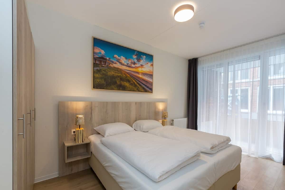 A modern hotel room with a large bed, bedside tables, a painting, and a view of the city.