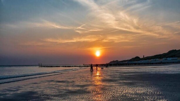 Ein Sonnenuntergang über einem Strand mit einem Steg, der sich ins Wasser erstreckt.
