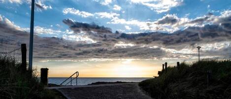 A paved pathway leading to a beach with a sunset in the background.