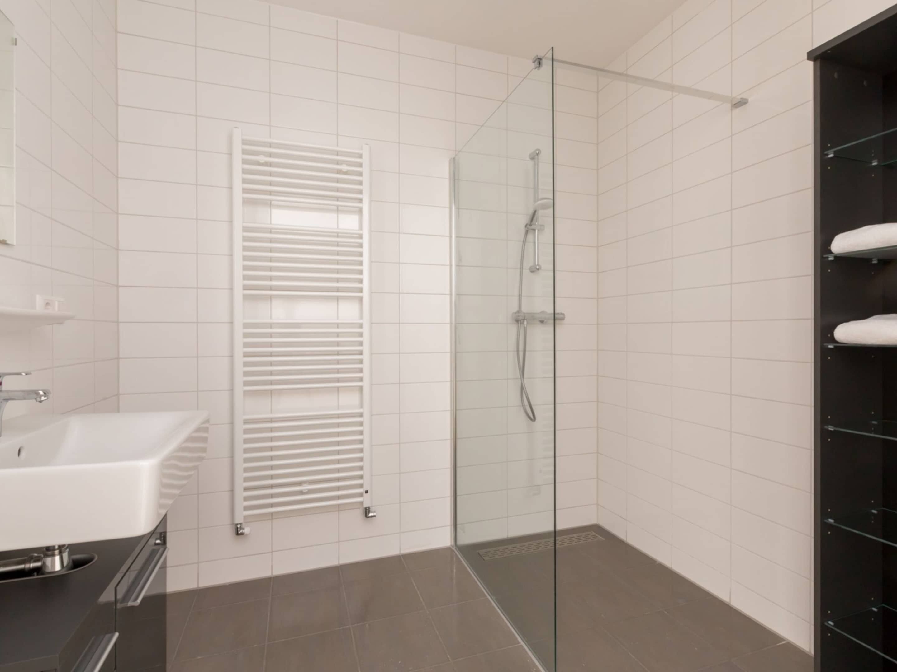 A modern bathroom with a glass-enclosed shower, a white sink, and a towel rack.