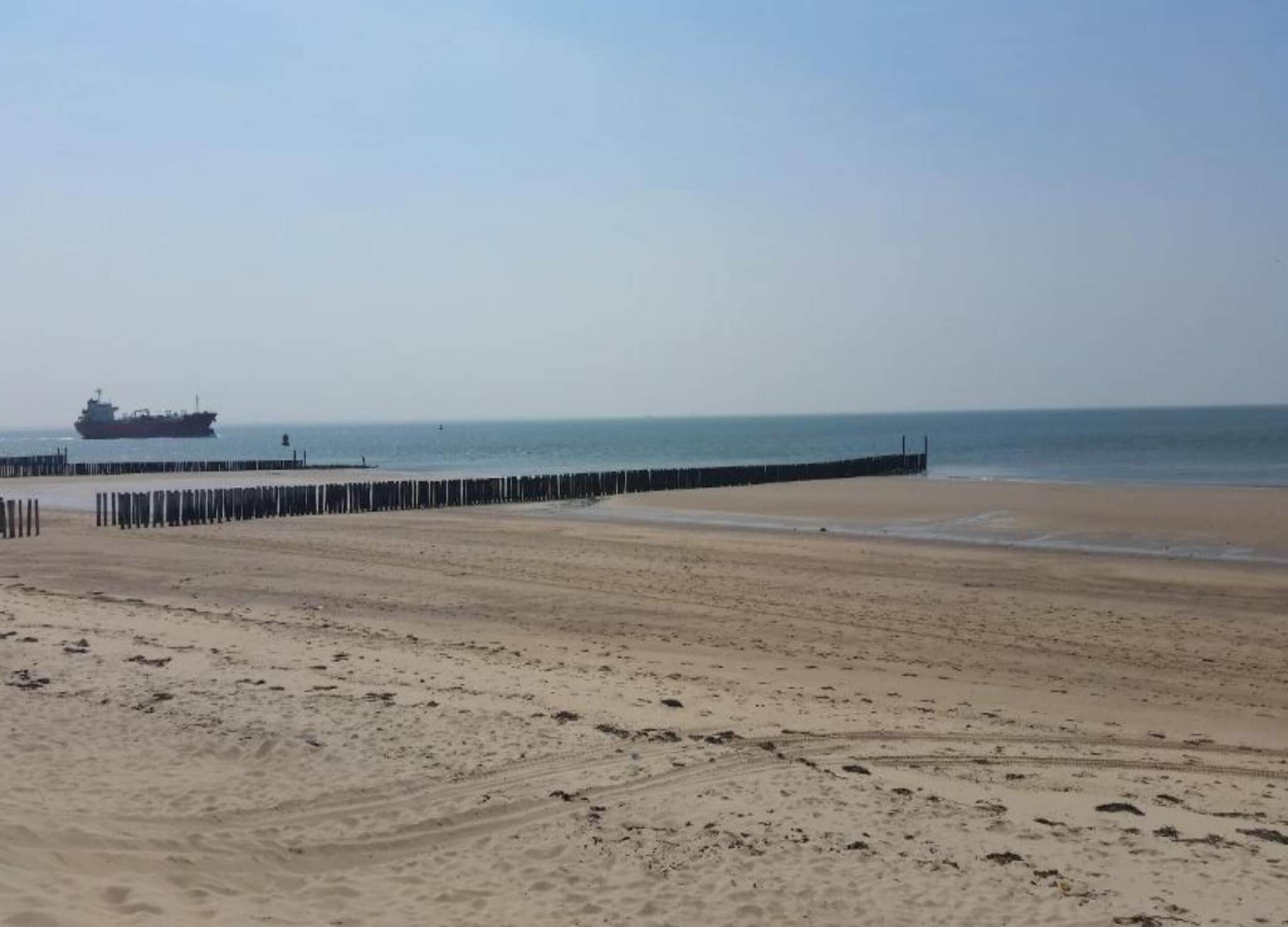 Une plage de sable avec une jetée en bois et un grand navire visible au loin.