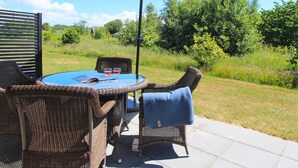 An outdoor patio with wicker furniture, a round table, and a large umbrella. - 4 Person Holiday Home in Ronne (Ronne)