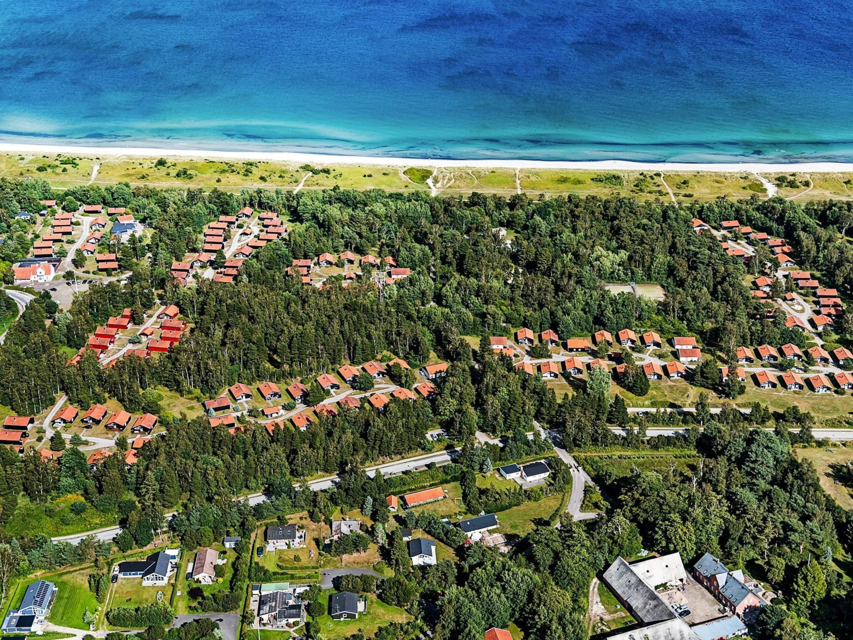 Oversigtsbillede af et kystnært boligområde med huse grupperet sammen, omgivet af tætte skove og en strand i baggrunden.