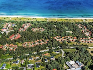 An aerial view of a coastal residential area with houses arranged in clusters, surrounded by dense forests and a beach in the background. - 6 Person Holiday Home on a Holiday Park in Vaeggerlose (Vaeggerlose)