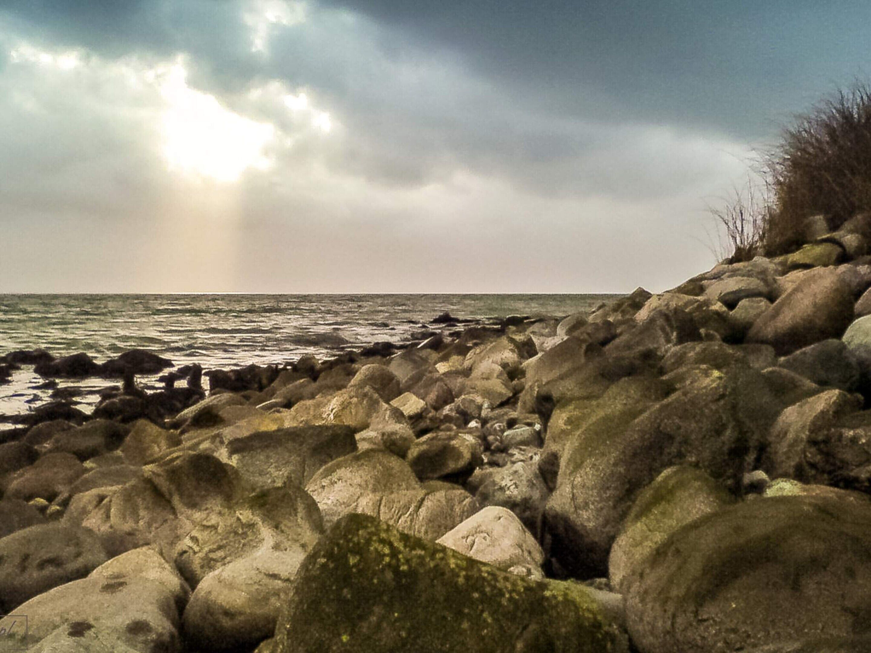 Une côte rocheuse parsemée de gros rochers, avec une vue sur la mer sous un ciel nuageux.