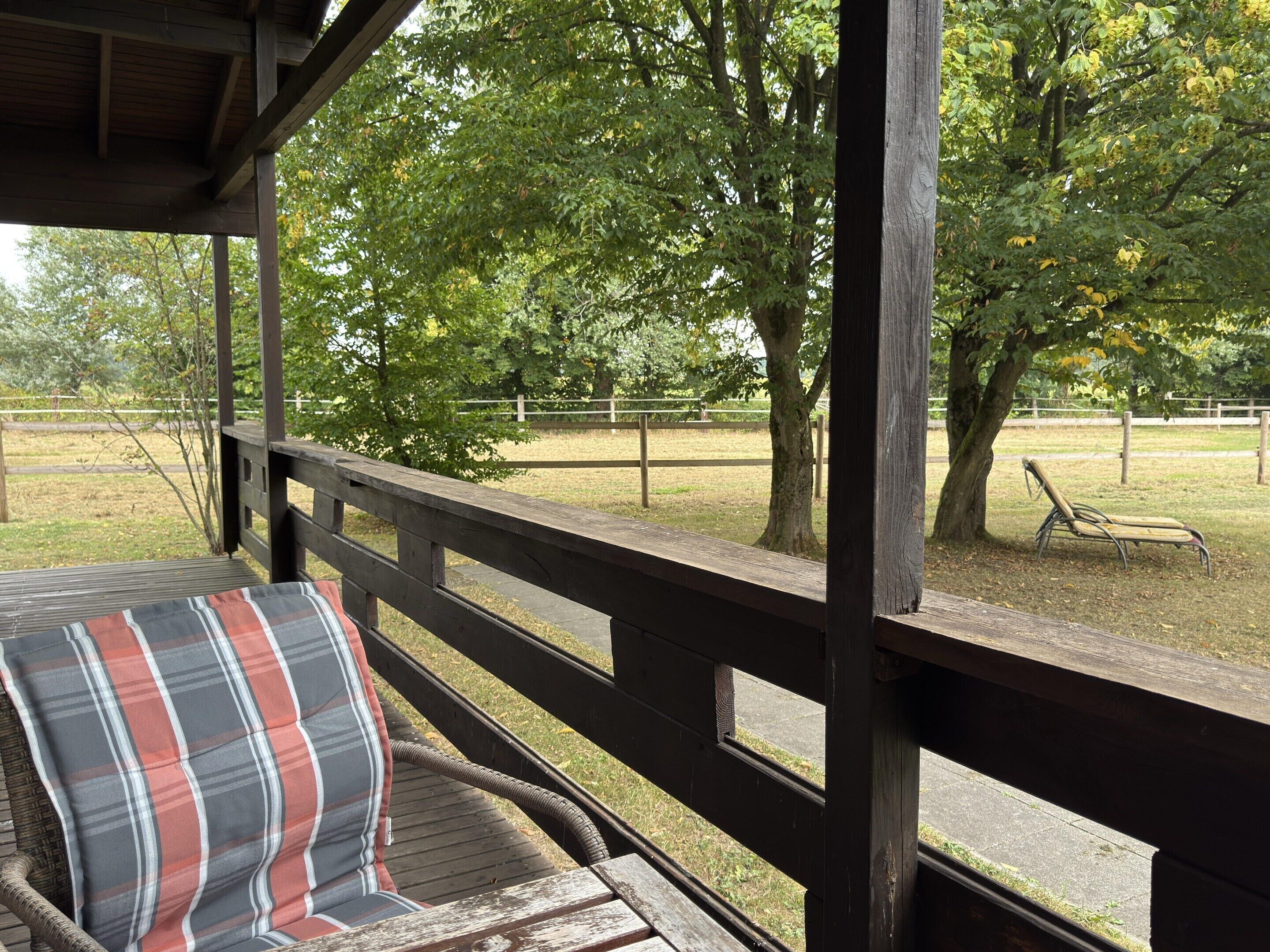 A covered outdoor seating area with a wooden bench and a plaid cushion.