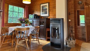 L’intérieur d’un chalet en bois comprend un coin repas, un poêle à bois et une fenêtre donnant sur un paysage verdoyant.