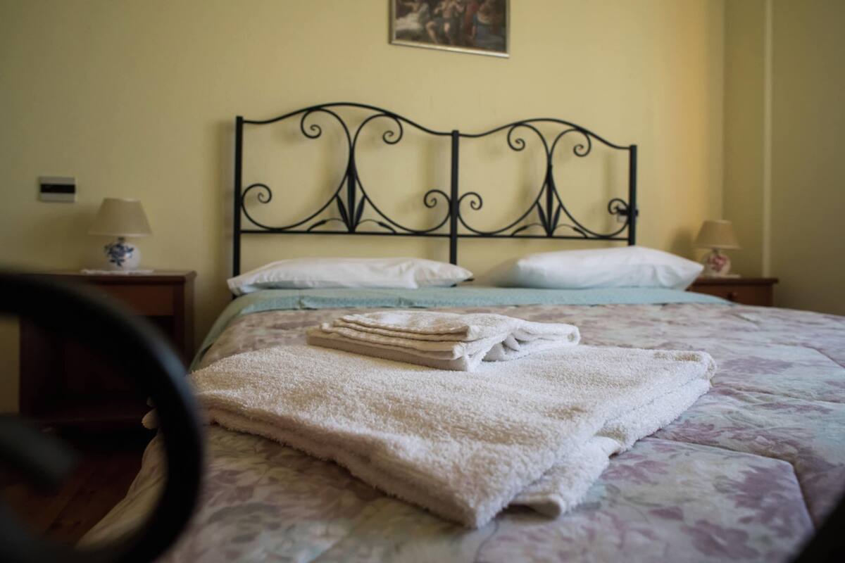 A neatly made bed with a floral bedspread, a folded towel, and a headboard with a decorative design.