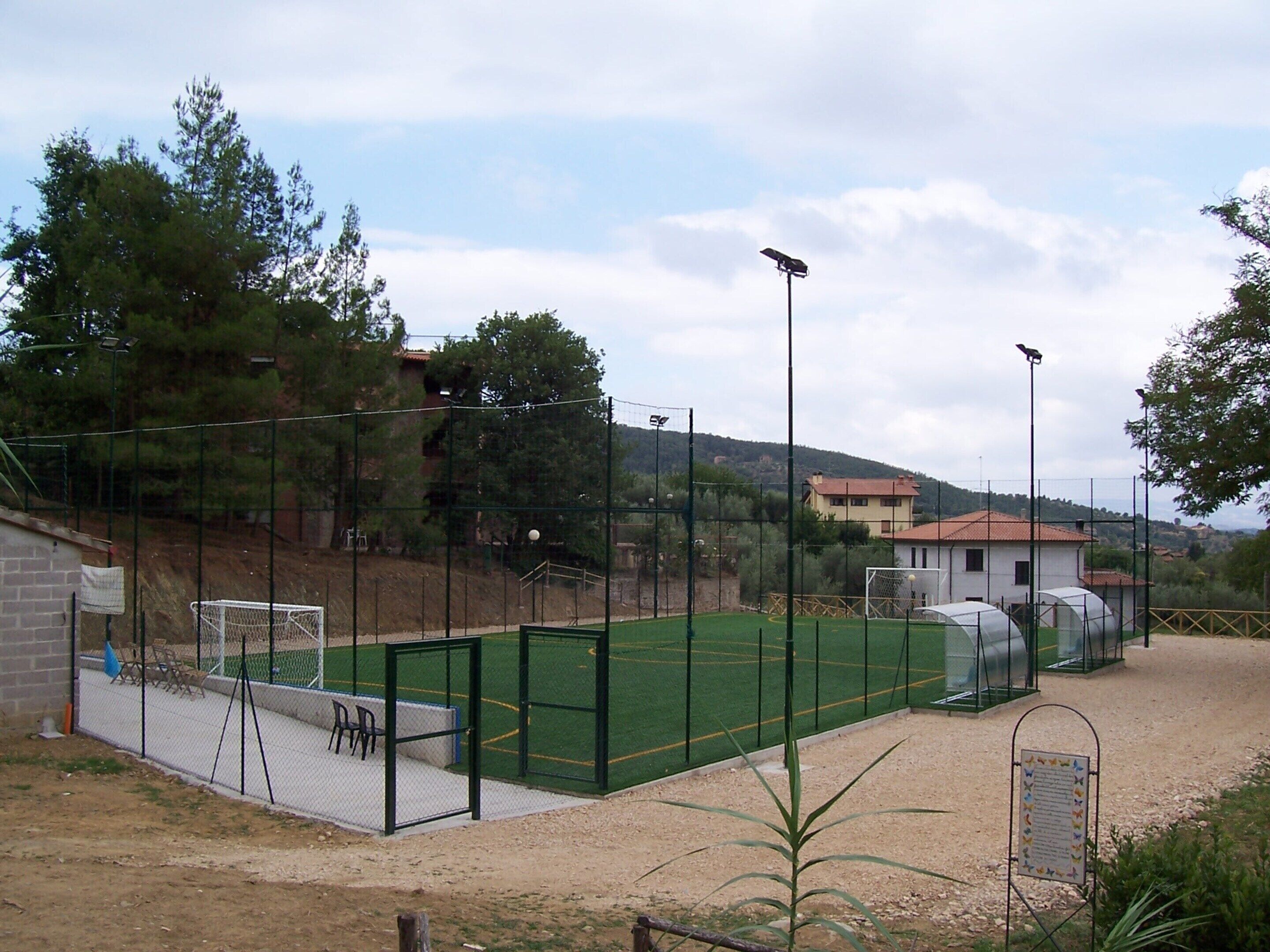 A fenced sports field with a goalpost, seating area, and a building in the background.