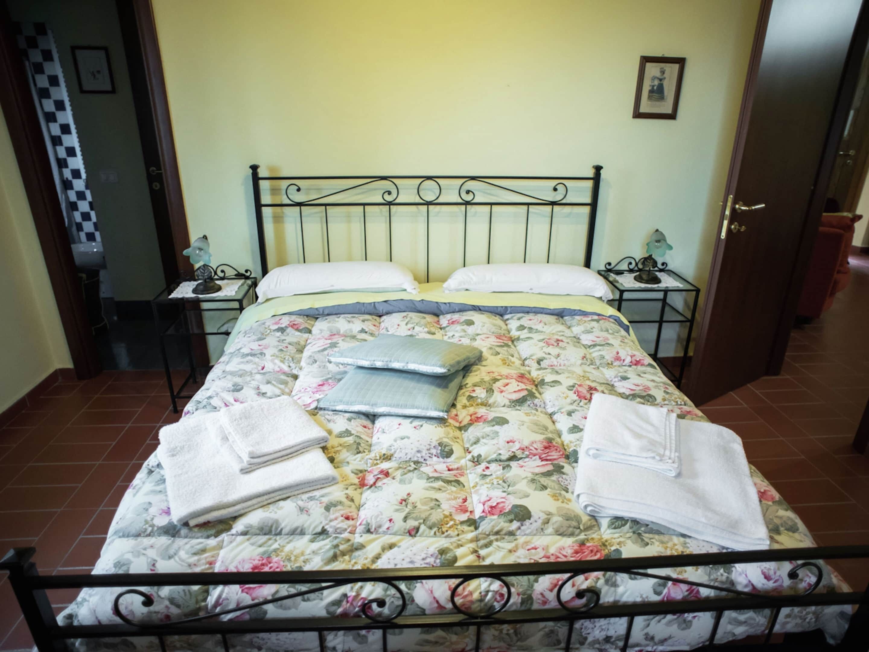 A bed with a floral comforter, two pillows, and two folded towels.