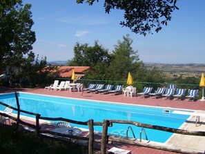 Ein Poolbereich mit Liegestühlen und Sonnenschirmen, umgeben von Bäumen und Blick auf die Landschaft.