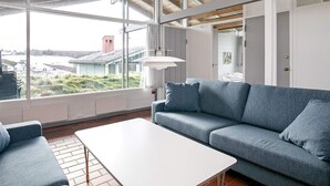 A modern living room with a grey sofa, a white coffee table, and large windows offering a view of the outside.
