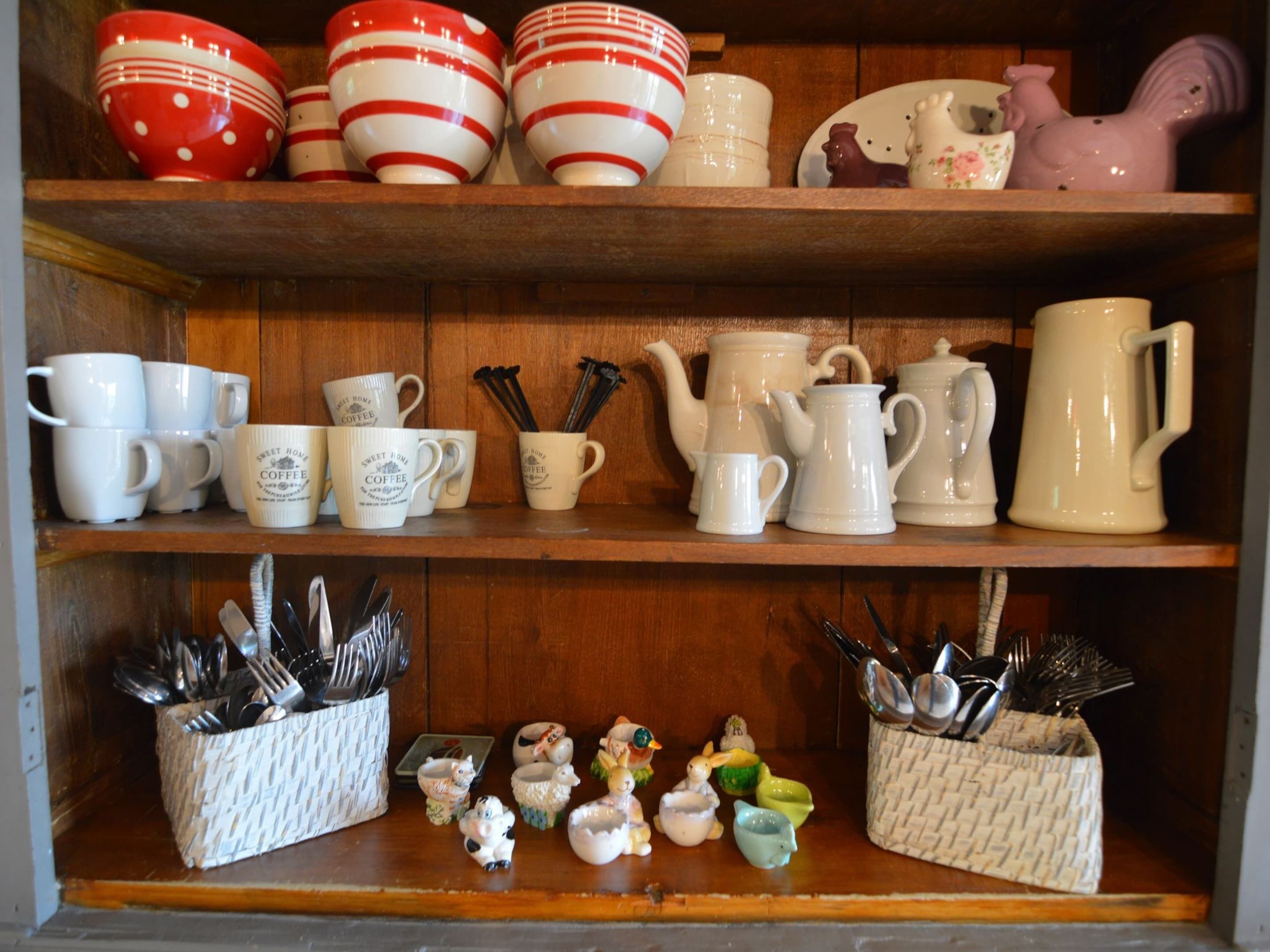 A shelf with various kitchenware, including cups, mugs, and teapots.