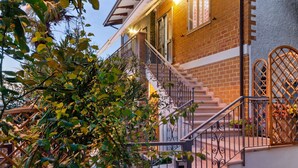 A brick house with a staircase leading to the entrance, surrounded by greenery. - Pleasant Apartment With Courtyard (Saludecio)