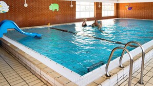 Piscina interna com um escorregador azul, parede de tijolos com murais de animais e chão de azulejos.
