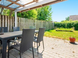 Un patio al aire libre con una mesa y sillas, una pérgola, una valla de madera y una zona ajardinada.