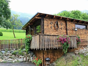 Eine rustikale Holzhütte mit Balkon, umgeben von Grünpflanzen und einer Steinmauer.