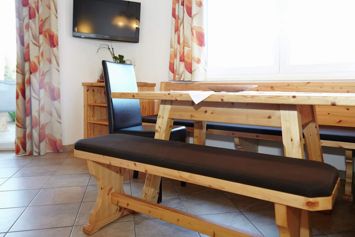 Un banc en bois avec un siège rembourré, un téléviseur fixé au mur et une plante posée sur une table.