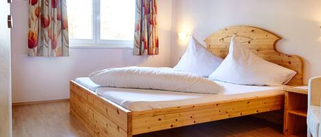 Una cama de madera con ropa de cama blanca en una habitación con suelo de madera y una ventana con cortinas florales.