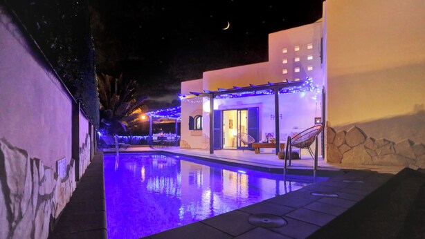 A nighttime pool area with a clear view of the pool, lounge chairs, and a building with a stone facade. - CASA MAY , LUXURY VILLA

 UNIQUE ONE OFF MOROCCAN VILLA

5 STARS  on Tripadvisor (Corralejo)