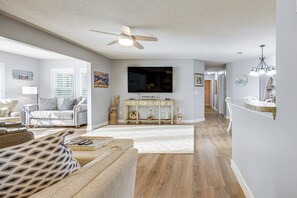 Un salon doté d’un ventilateur de plafond, d’un téléviseur à écran plat, d’une console en bois et d’un tapis blanc.