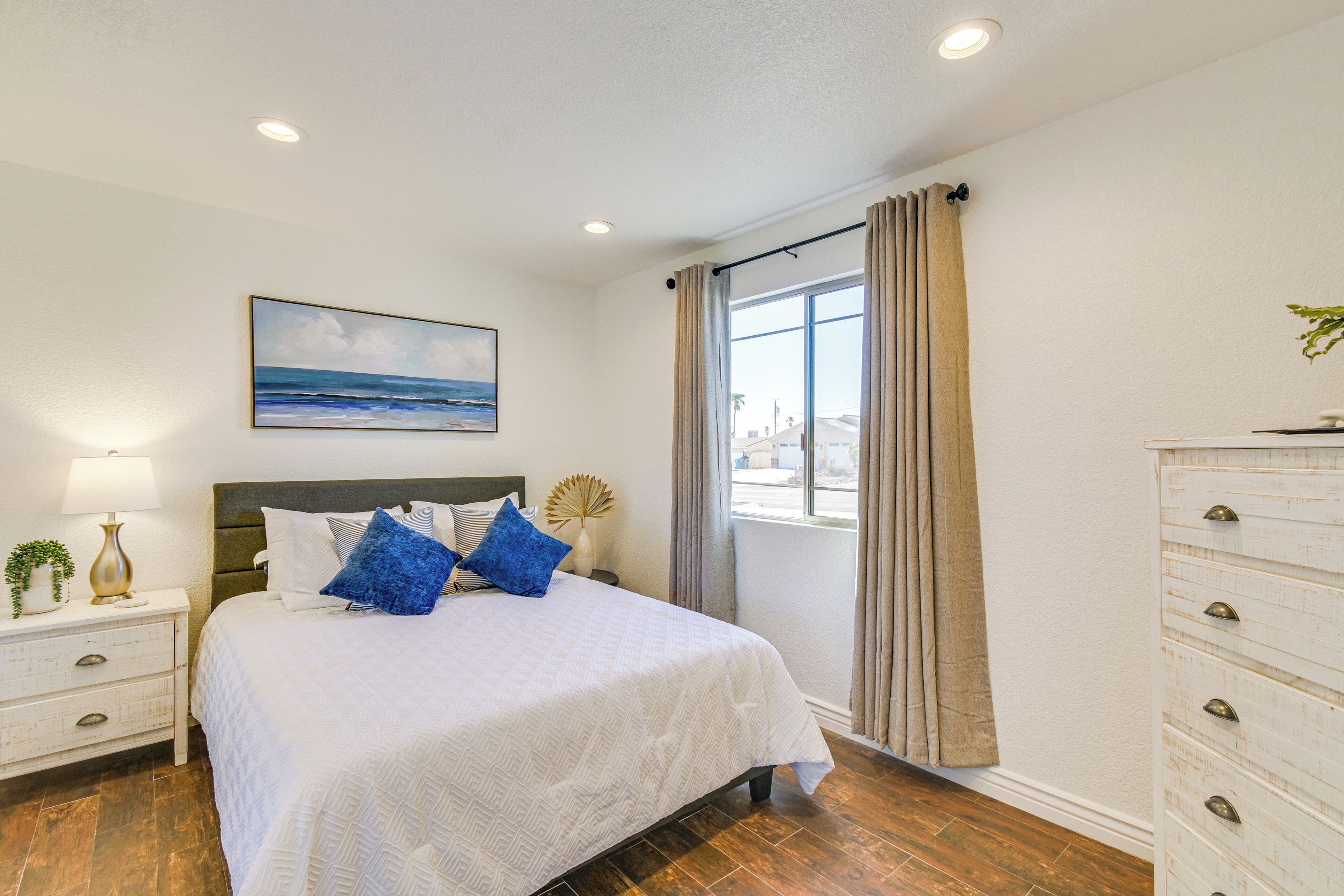 Un dormitorio ordenado con cama, mesita de noche, lámpara y un cuadro en la pared.