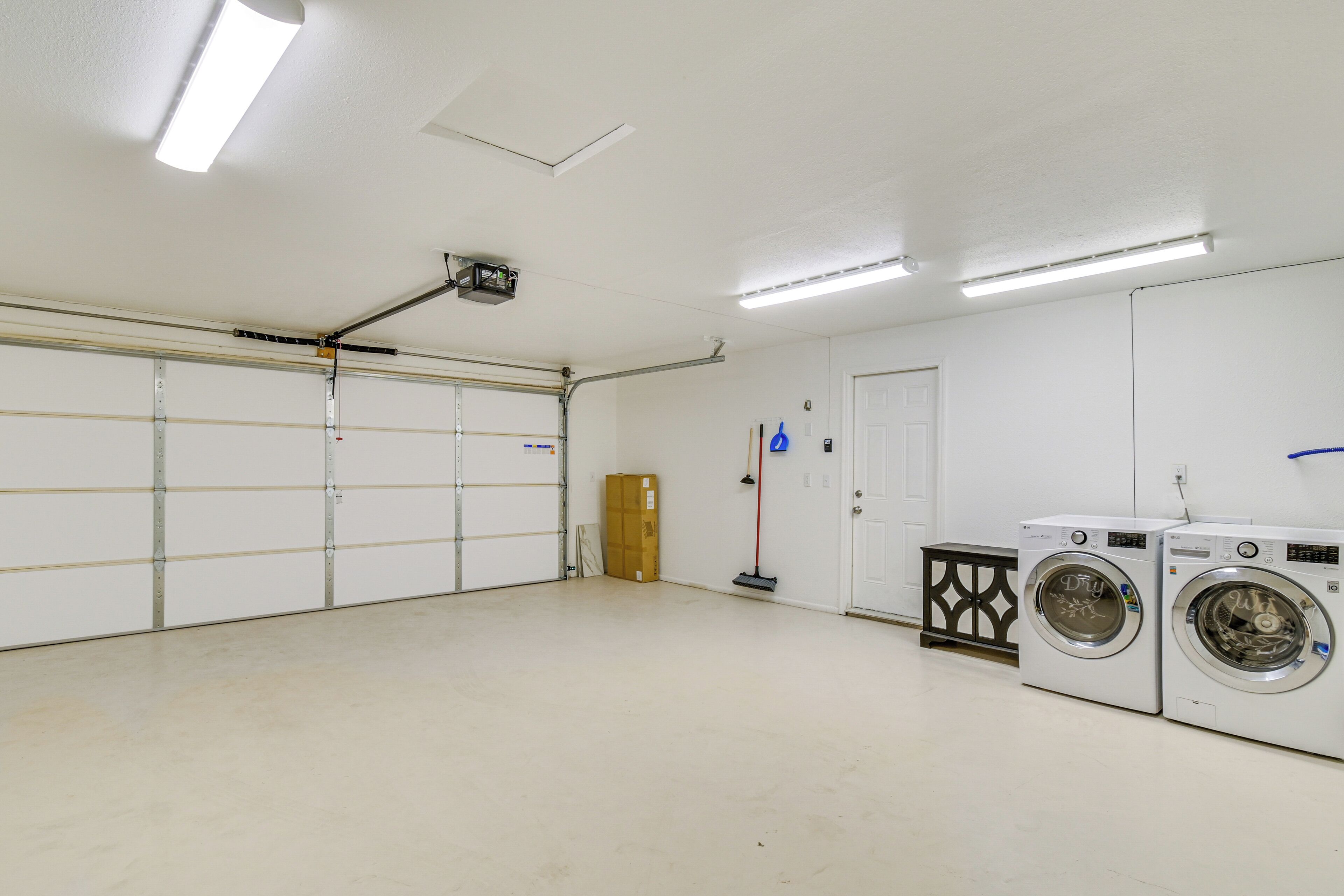 A clean, well-lit laundry room with two front-loading washing machines, a broom, and a cardboard box.