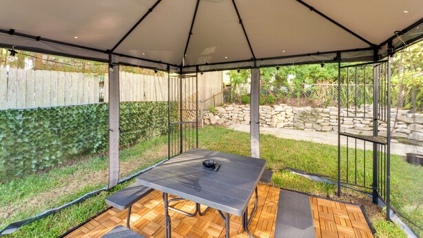 A covered patio with a table and chairs, surrounded by a wooden deck and a stone wall. - Daytona Beach Studio: Walk to Boardwalk + Pier! (Daytona Beach)