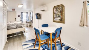 A hotel room with a bed, a dining area with a table and chairs, an air conditioning unit, a painting, and an exit sign. - Daytona Beach Studio: Walk to Boardwalk + Pier! (Daytona Beach)