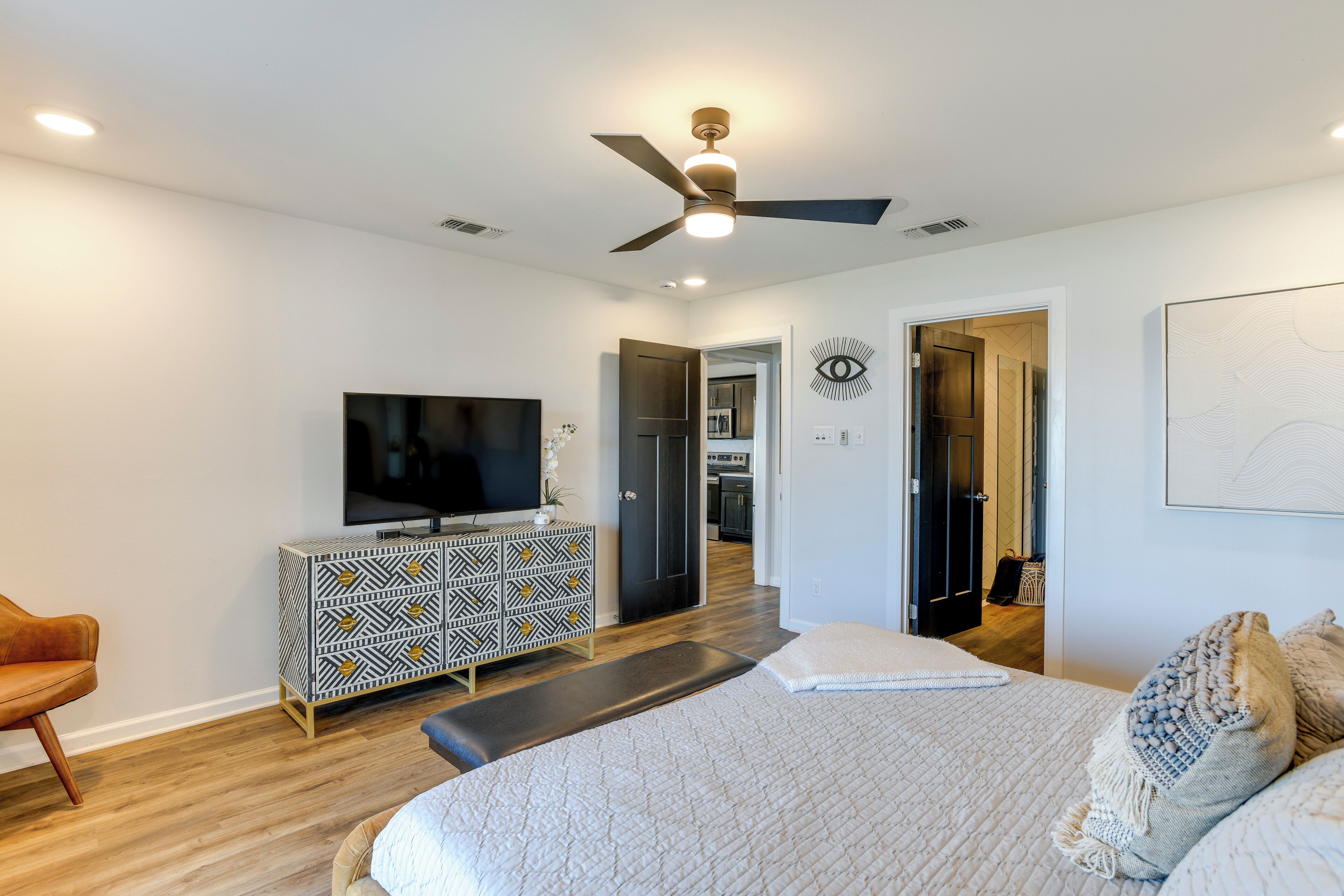 A modern bedroom with a bed, a TV, a patterned dresser, and a ceiling fan.