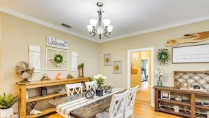 A dining area with a wooden table, white chairs, and a chandelier. There are decorative items on the walls and a 'Welcome' sign. - Georgia Countryside Home: 3 Mi to Wild Adventures! (Valdosta)