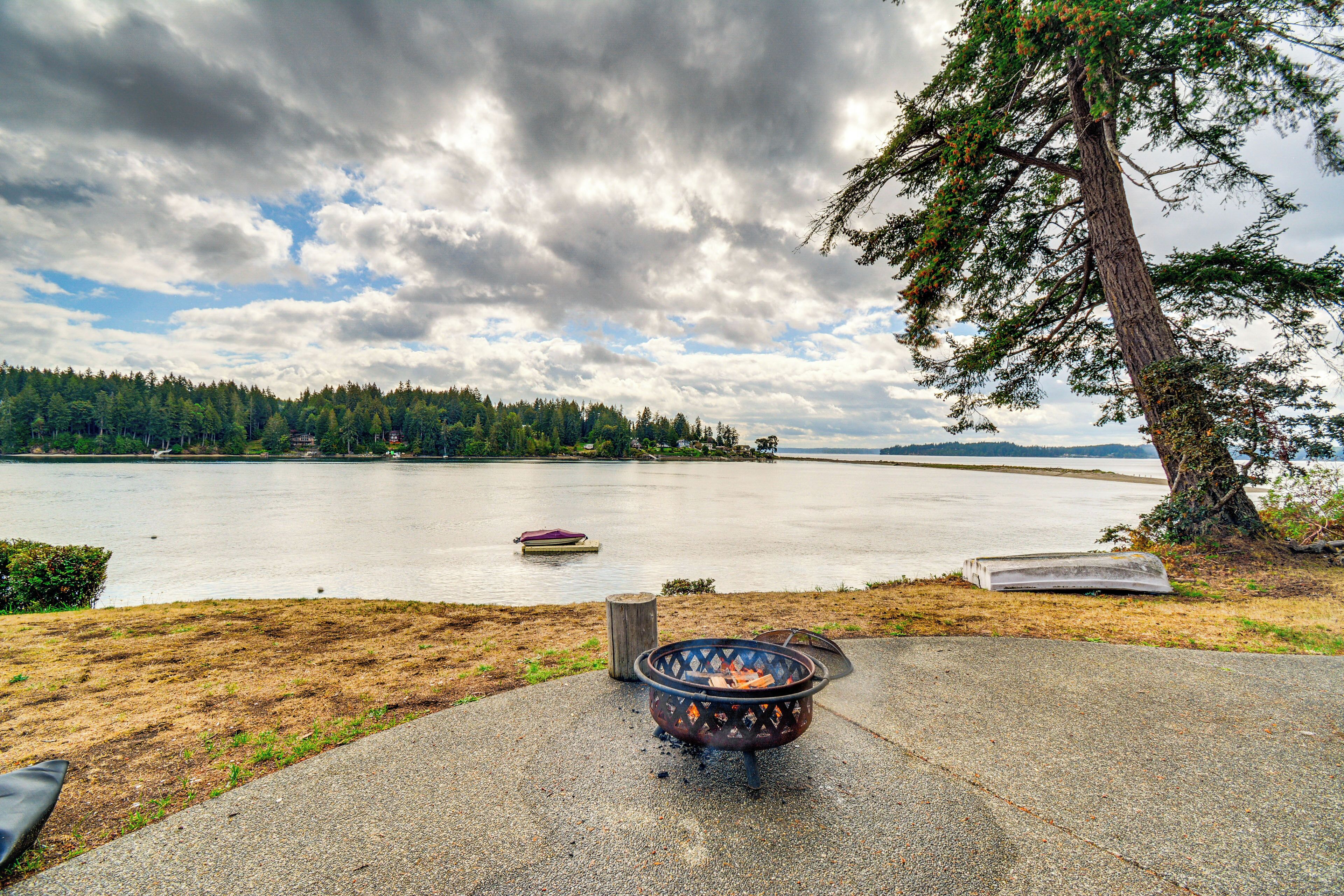A lakeside view with a fire pit, a boat, and a forested shoreline.