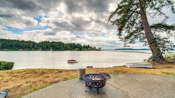 A lakeside view with a fire pit, a boat, and a forested shoreline.