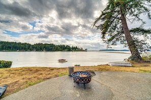 A lakeside view with a fire pit, a boat, and a forested shoreline.